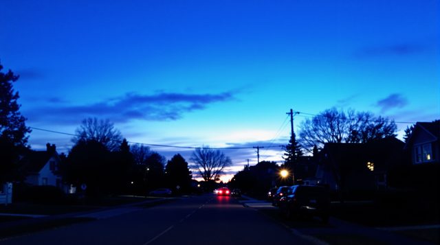 Blue Hour example: a quiet suburban street just after sunset, deep blue sky, one warm lit window