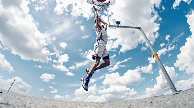 Worm's-Eye Low Angle example: looking up from the pavement at a basketball player mid jump, the hoop and sky behind