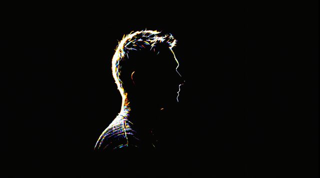 Rim Light Kicker example: a man's head and shoulders in profile facing right against a pure black background, a soft white glow outlining the back of his head and shoulder from a light behind him, his face dimly visible, no streaks