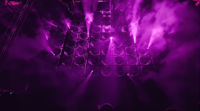 Dubstep example: a towering speaker wall throbbing with violet light in a warehouse rave, bass shockwave in smoke