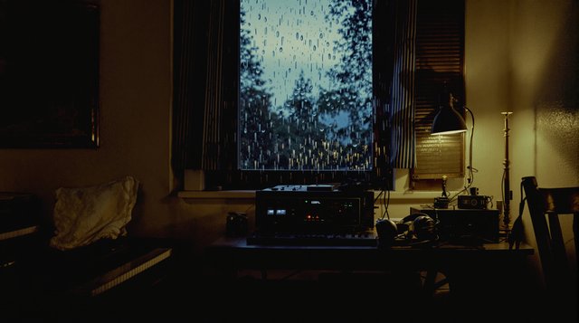 Lo-fi Hip Hop example: an electric piano, headphones and a cassette deck in a small bedroom at dusk, rain on the window, a desk lamp glowing