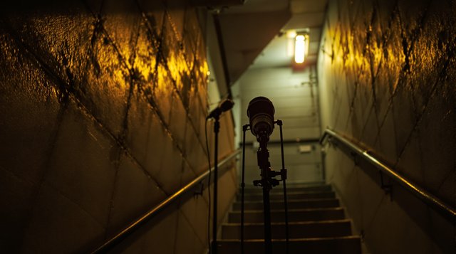 UK Drill example: a microphone on a stand in a cold concrete stairwell of a tower block at night, harsh fluorescent light