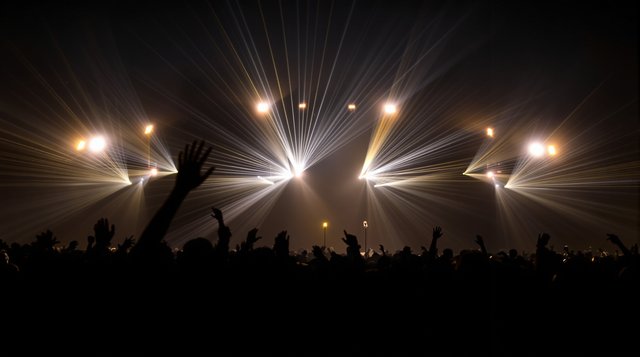 Vocal Trance example: a lone microphone glowing on a vast festival stage, laser beams sweeping a night sky, arms raised as silhouettes far below